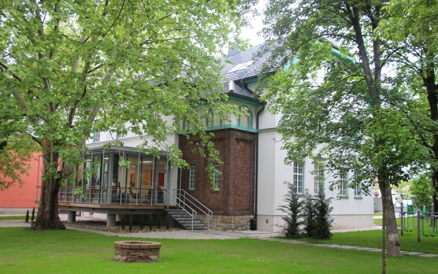 A központ épülete a zöld udvarral, fehér homlokzat és téglaszínű toldalék